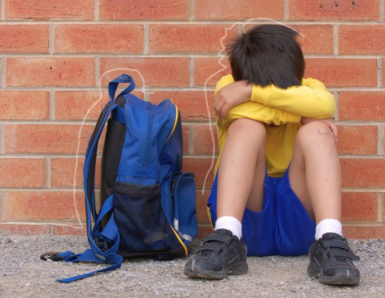 Child in school uniform slumped against a wall and sad